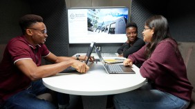 Three students using their laptops and collaborating on a group project in a study booth